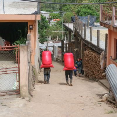 Farmers walking the dirt roads of La Libertad with large mylar bags filled with dried green coffee strapped to their backs. Huehuetenango, Guatemala.